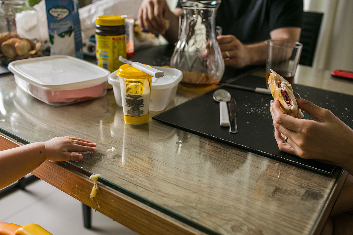 mãos da família na hora do café da manhã, com a banana do bebê escorrendo na lateral da mesa, por adrianacostafotos