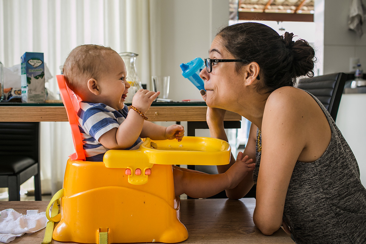 Mãe dando água para seu bebê que está super feliz com a brincadeira que ela faz, por adrianacostafotos