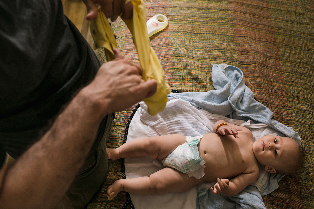 pai preparando a roupa para colocar no seu bebê em foto de Adriana Costa