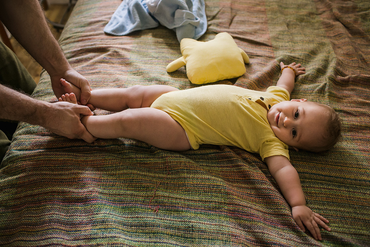 pai brincando com seu bebê de escorregá-lo pela cama em foto de Adriana Costa