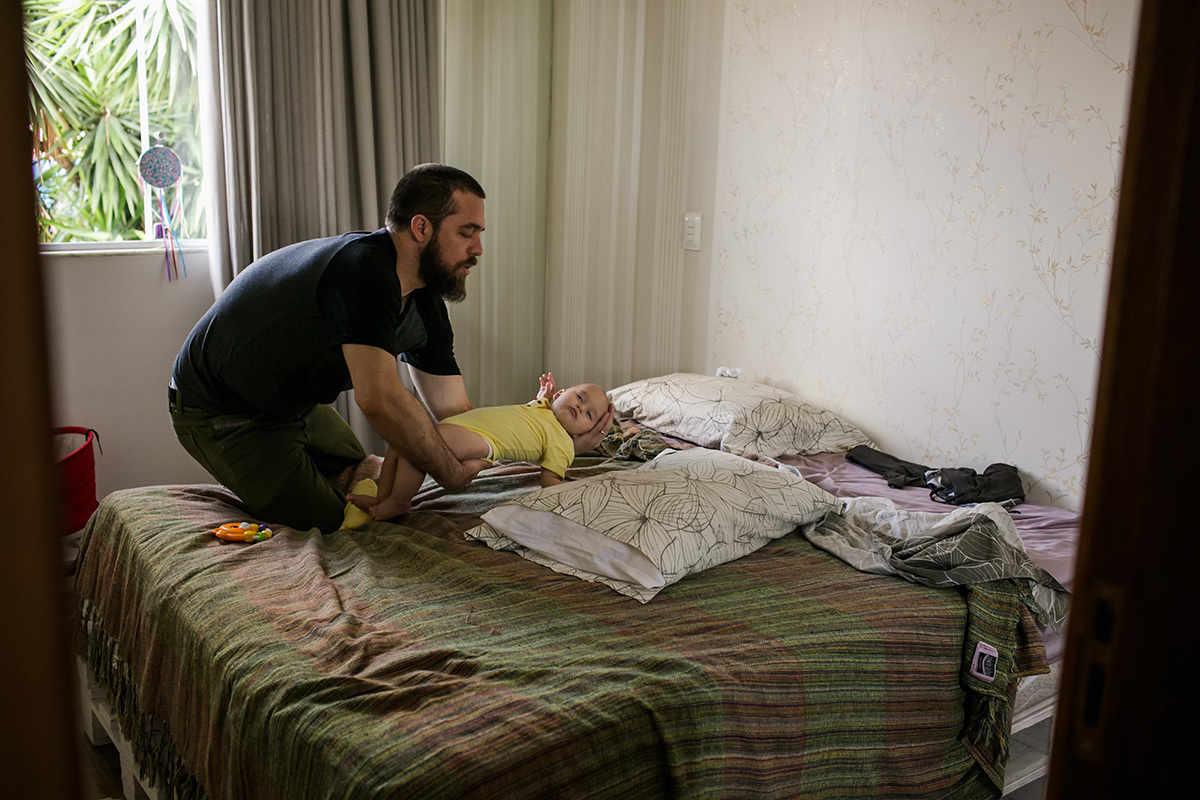 pai colocando seu bebê que dormiu com o maior cuidado na cama para não acordá-lo, por adrianacostafotos