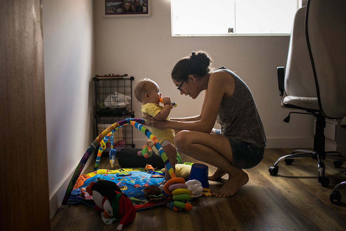 mãe colocando seu bebê para brincar no tapete de atividades que está no escritório em que ela trabalha