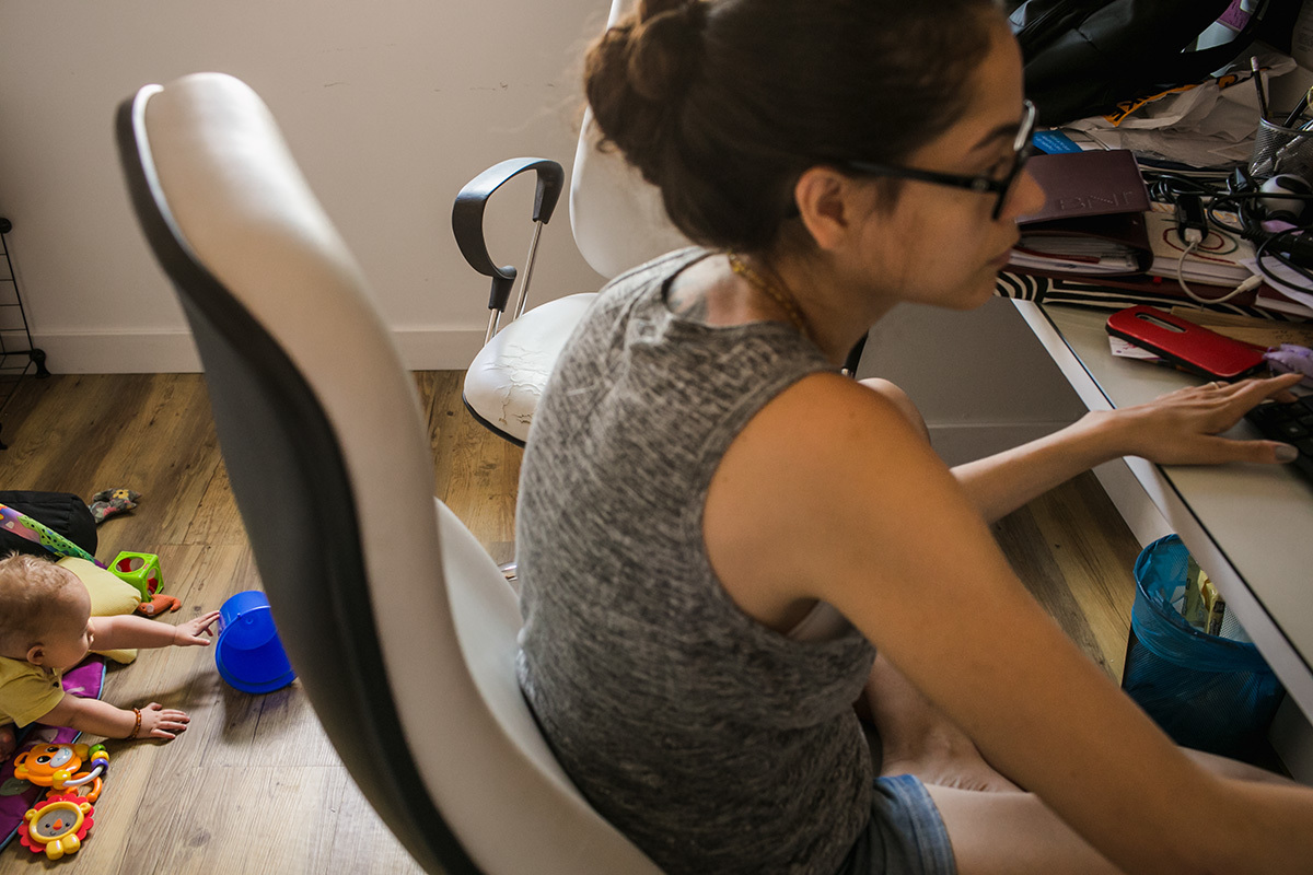 mãe trabalhando enquanto seu bebê brinca no tapete de atividades, por Adriana Costa