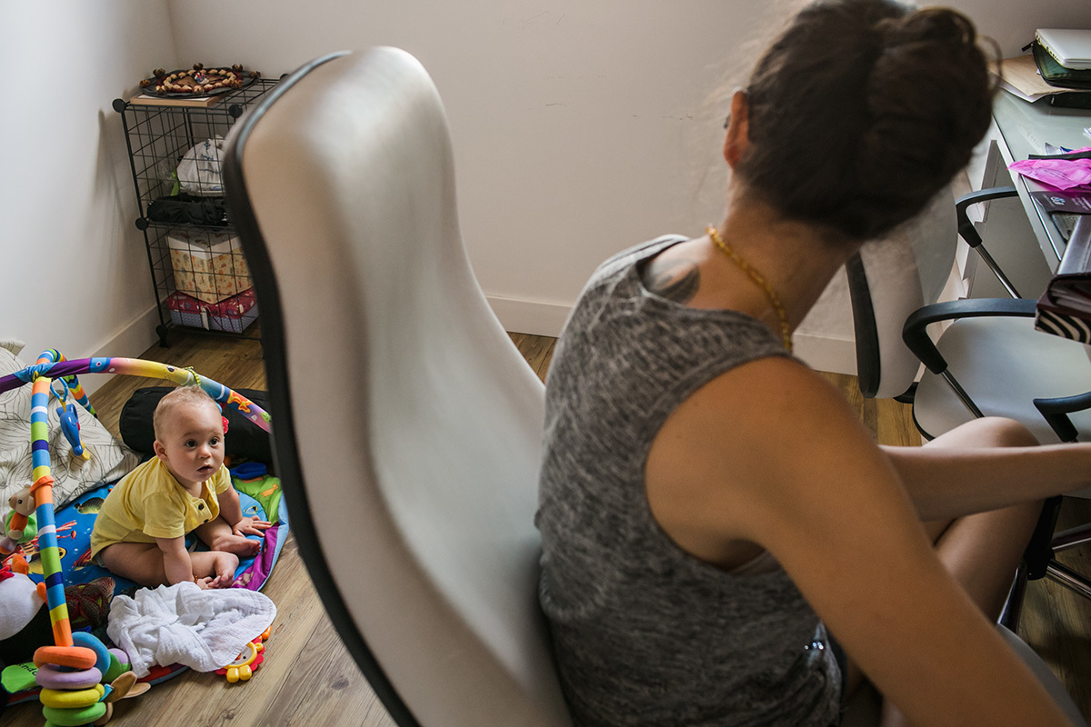 mãe olhando para seu bebê que brinca ao seu lado enquanto ela trabalha