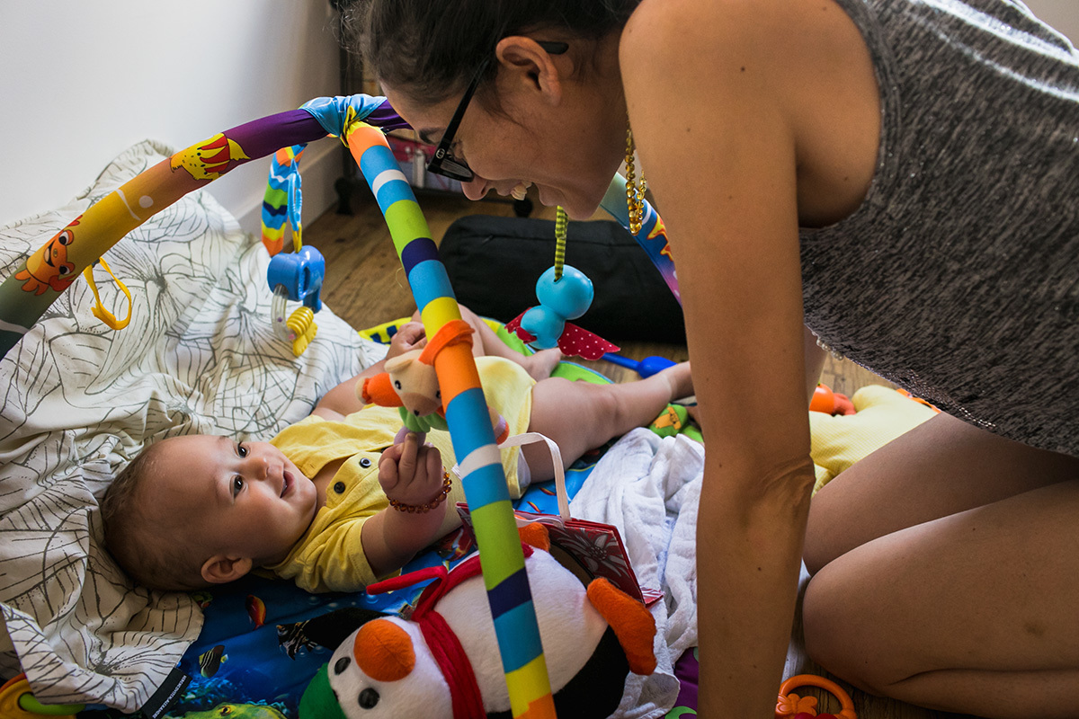 mãe rindo para seu bebê que está brincando em seu tapete de atividades, por adrianacostafotos