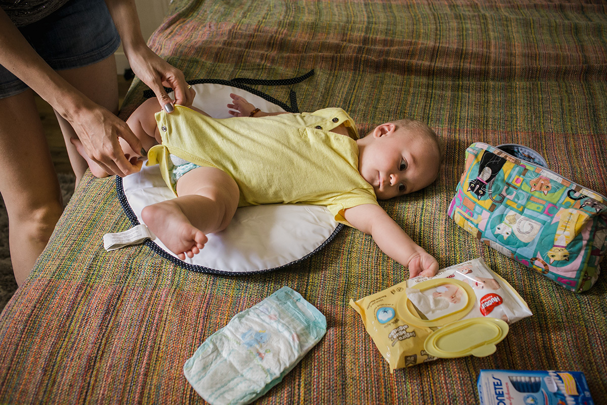 mãe trocando a fralda do bebê e ele tentando pegar os objetos em volta