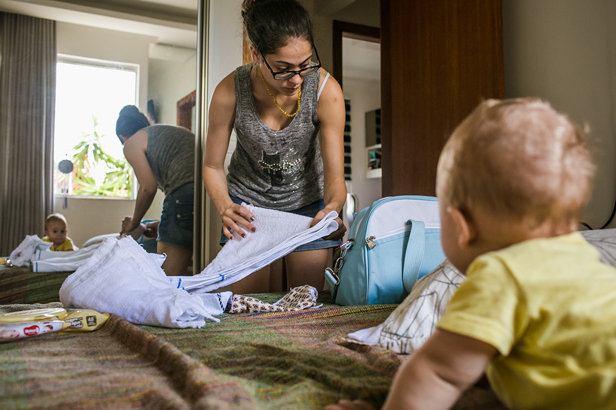 Foto de Adriana Costa do bebê observando sua mãe arrumar a bolsa dele para sair