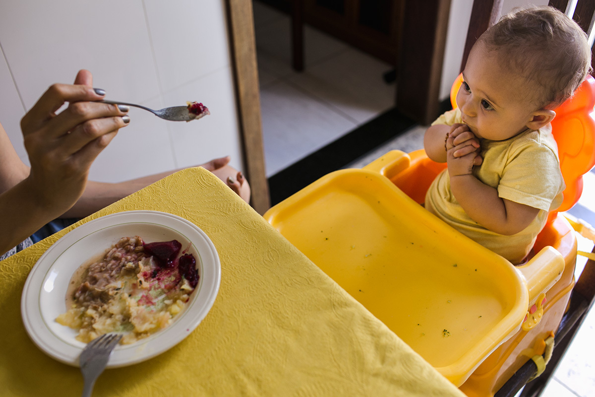 bebê entrelaçando as mãos aflita diante da colher de comida, por adrianacostafotos