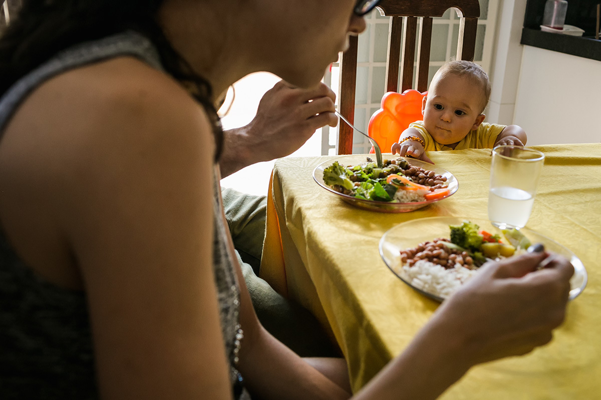 bebê tentando puxar o prato do pai na hora do almoço, por adrianacostafotos