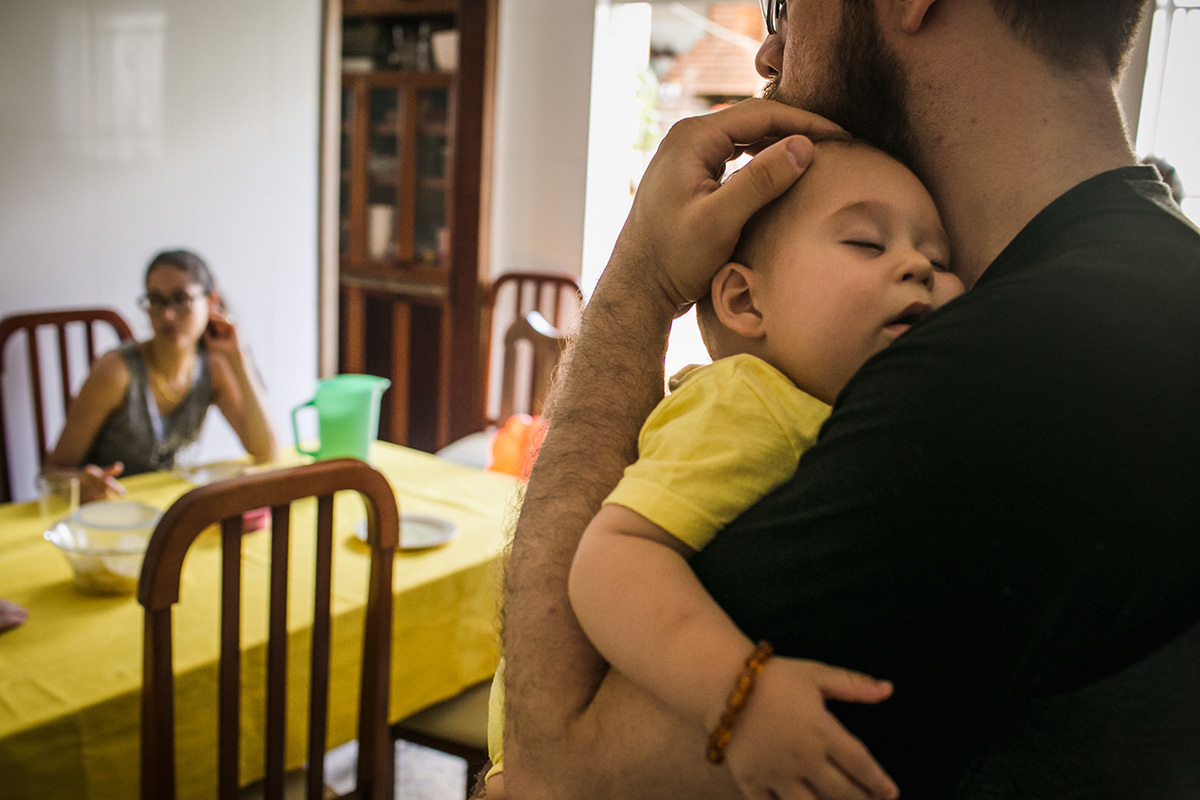 Foto de Adriana Costa do pai fazendo o bebê dormir enquanto a mãe almoça