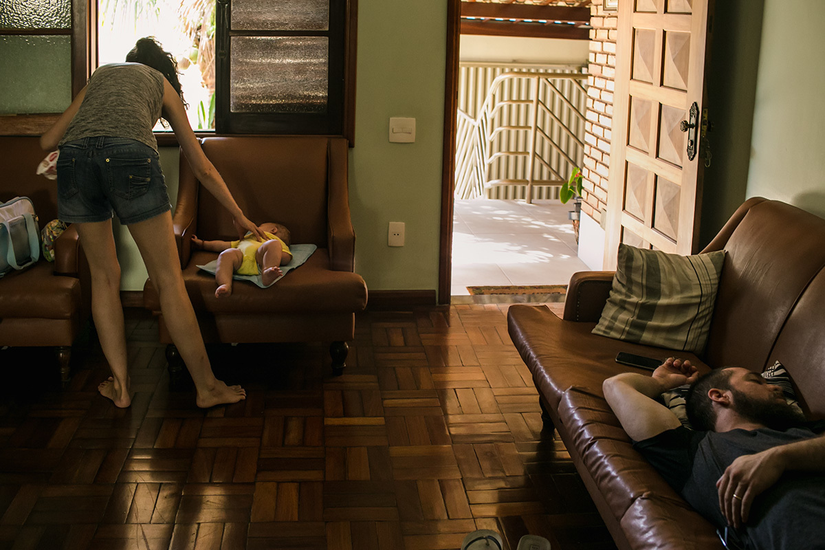mãe trocando a fraldo do bebê enquanto o pai dorme