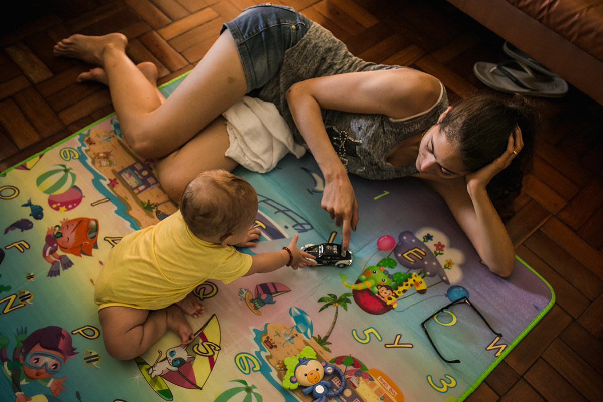 mãe brincando de carrinho com seu bebê no chão em foto de Adriana Costa