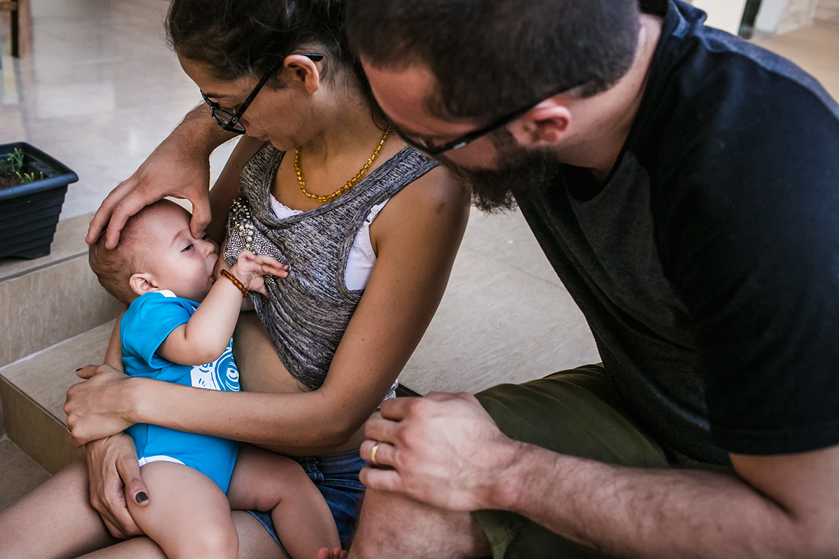 foto de Adriana Costa do pai acarinhando o filho que amamenta na mãe