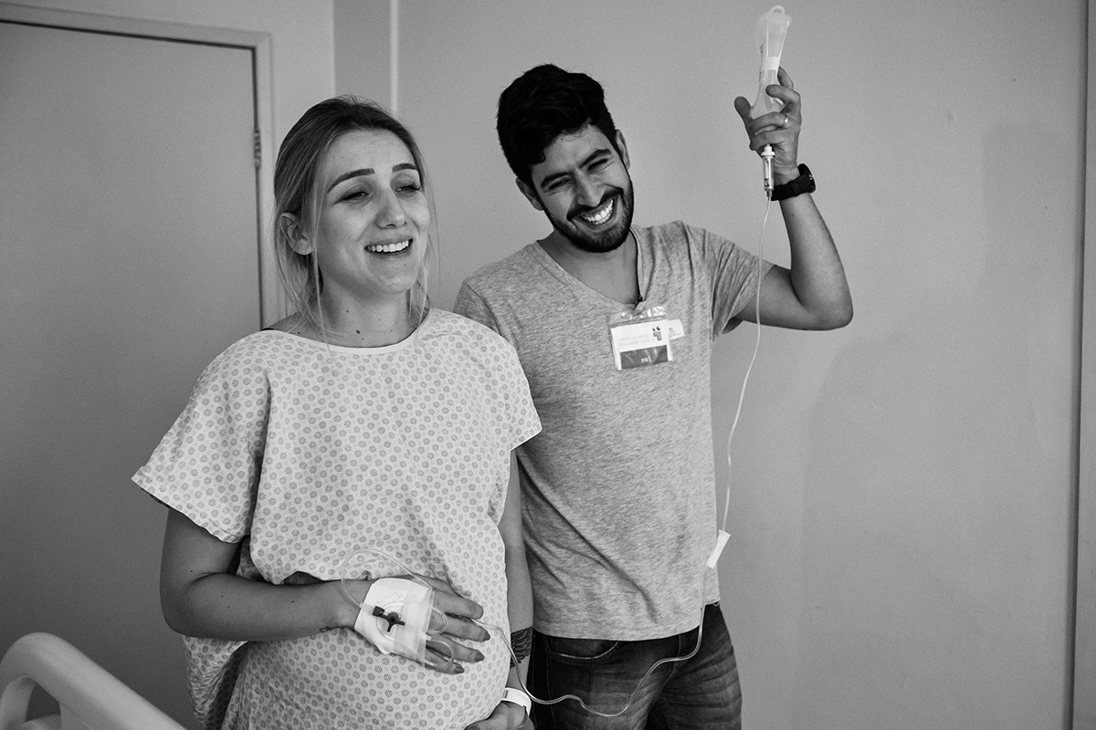 casal caminhando sorrindo no quarto da maternidade para ajudar no trabalho de parto, por adrianacostafotos