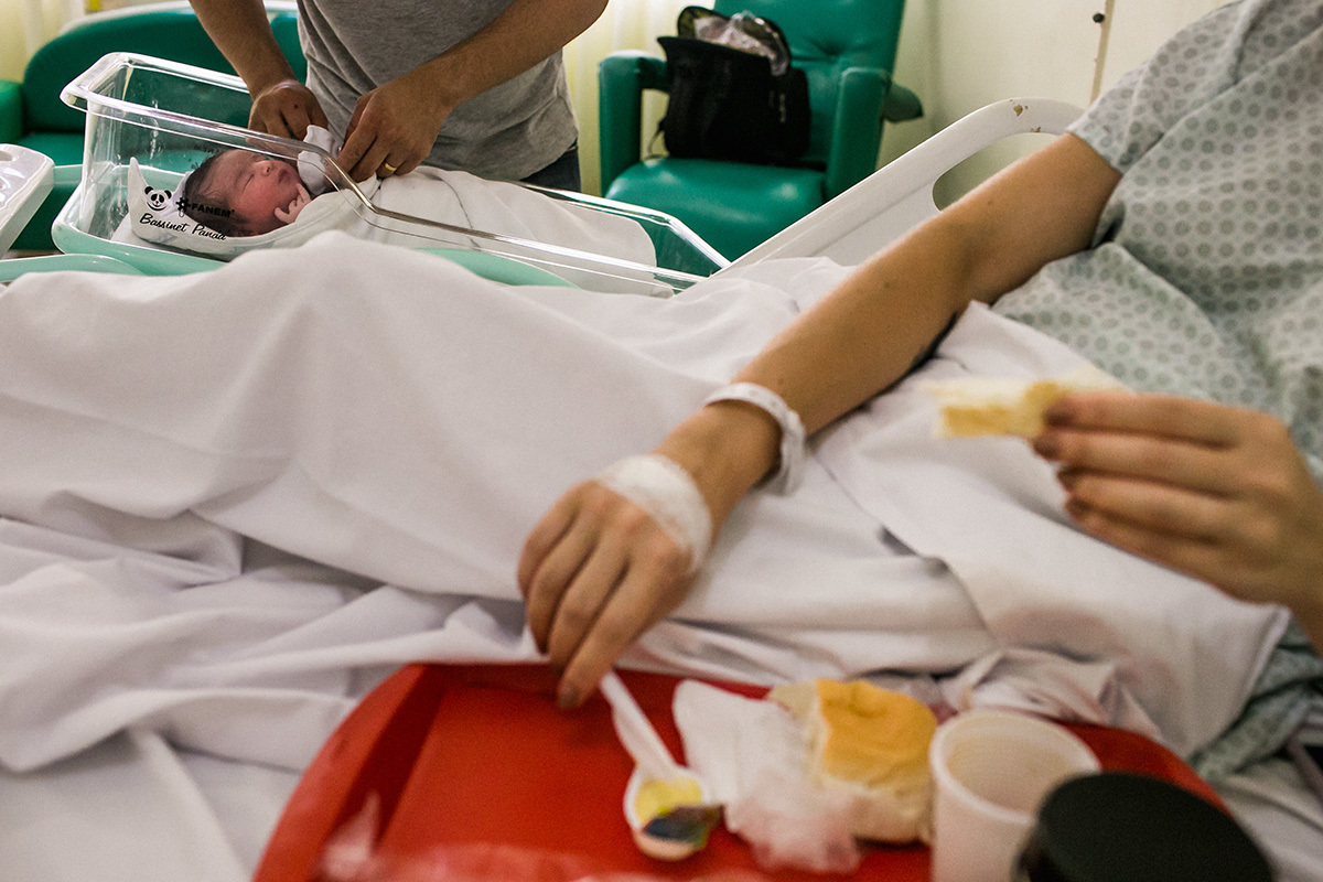 mãe logo após o parto normal fazendo um lanche enquanto o pai cuida do bebê