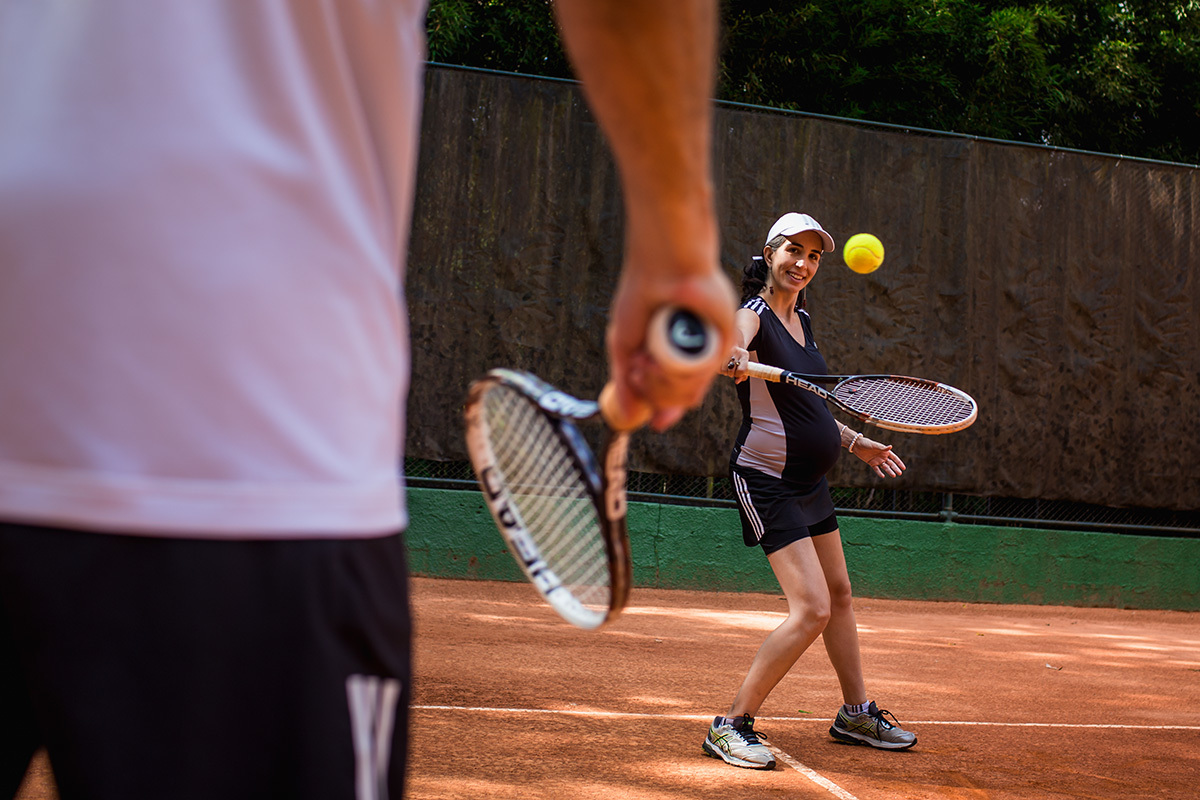 gestante rebatendo a bola de tênis para seu marido