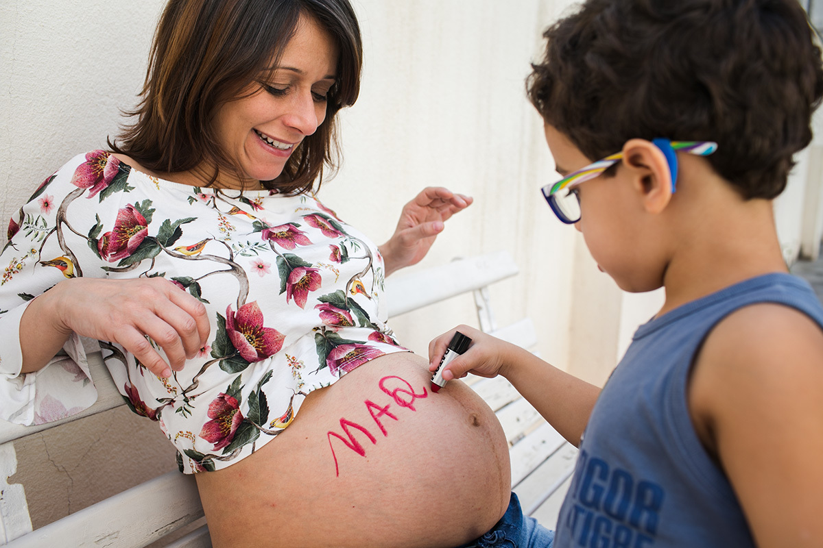 menino escrevendo na barriga da tia o nome da prima