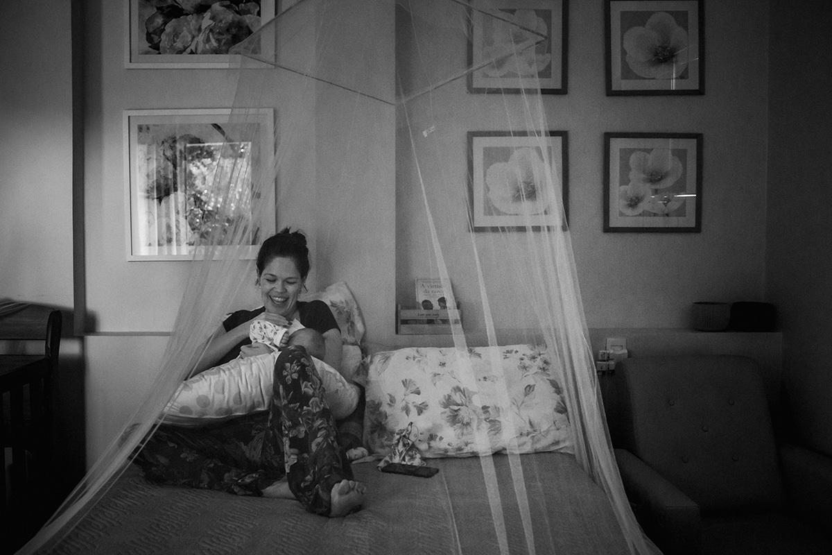 mãe amamentando no quarto de casal sob tela mosquiteira, por adrianacostafotos