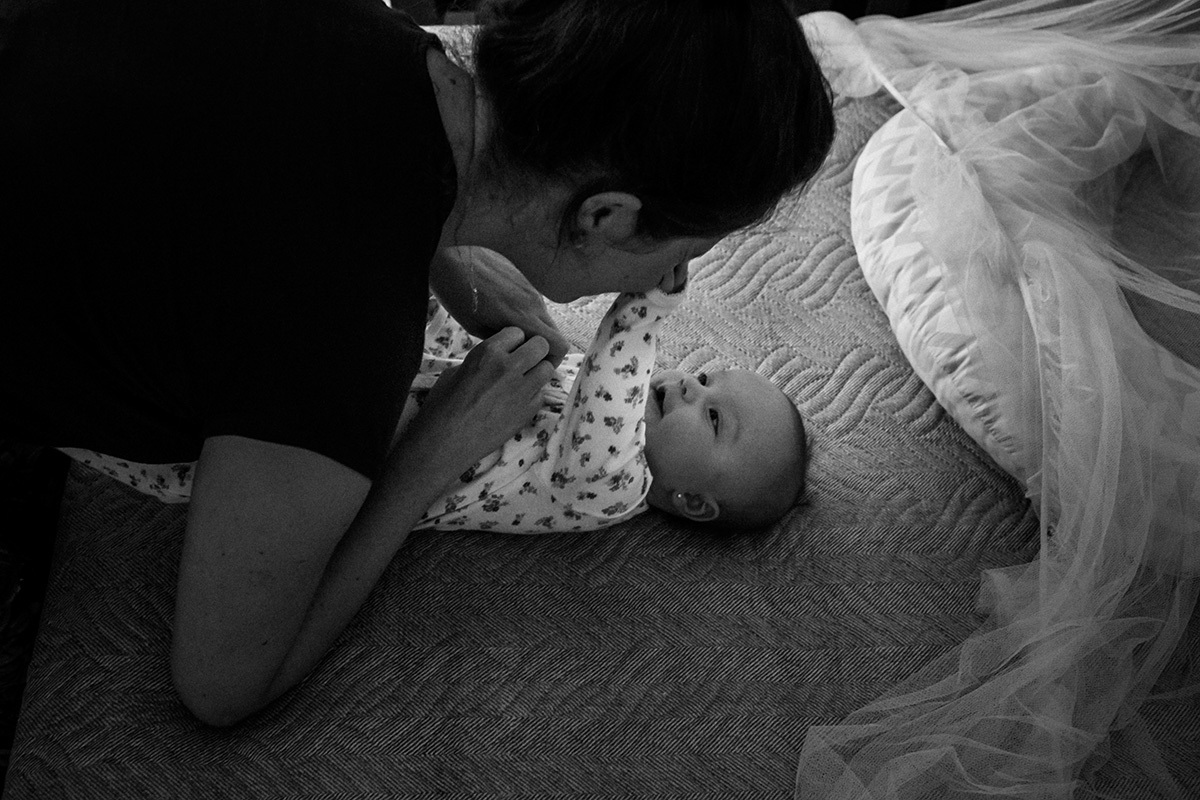 Mãe brincando com sua bebê de cinco meses na cama em uma foto de Adriana Costa