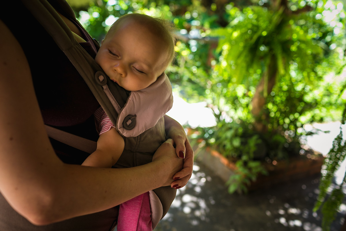 bebê dorme no colo da mãe, no quintal da casa, por Adriana Costa