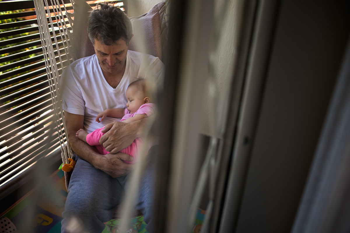 Foto de Adriana Costa do pai na varanda com a filha dormindo no seu colo