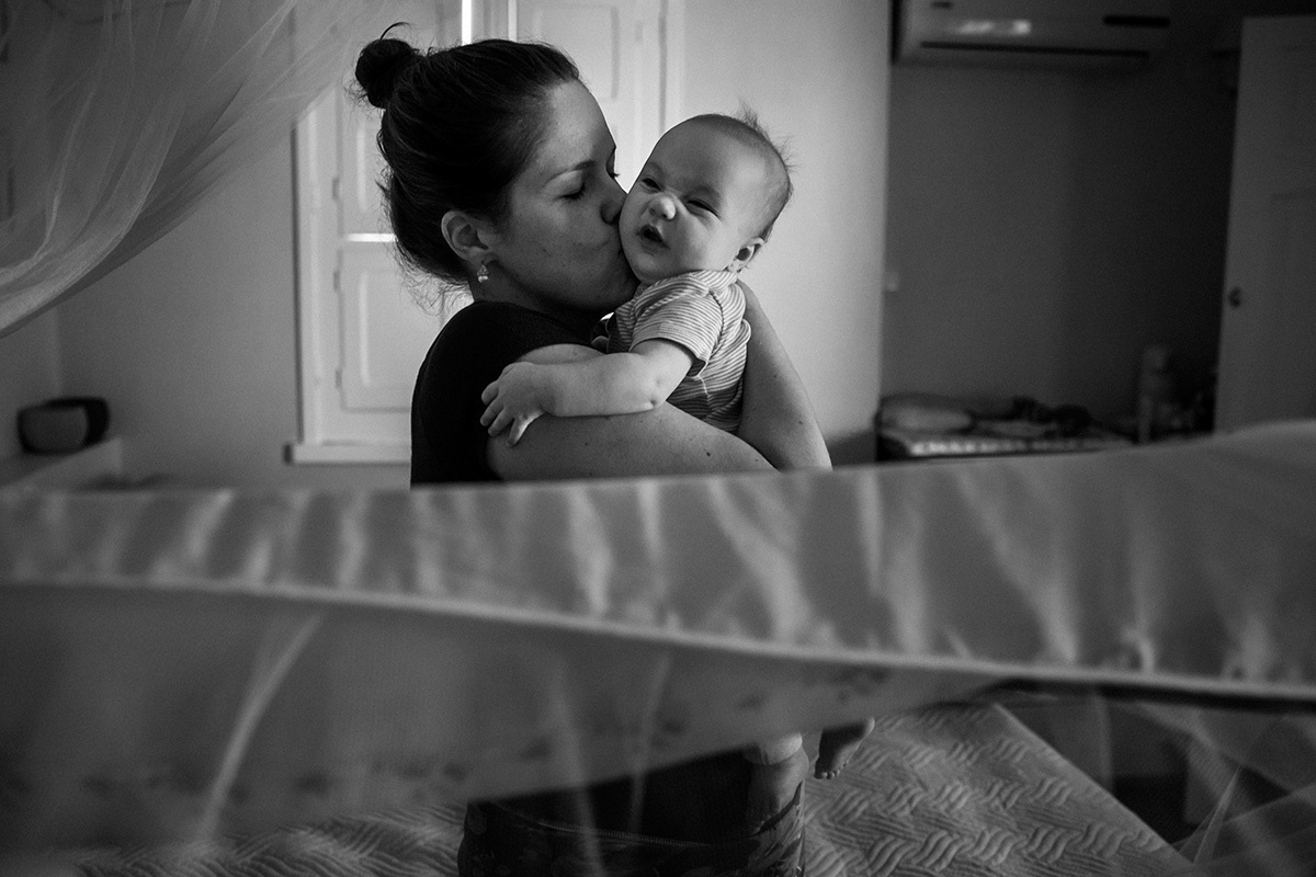 bebê franzindo o nariz sob o abraço da mãe que a pegou no colo depois que ela acordou, por Adriana Costa