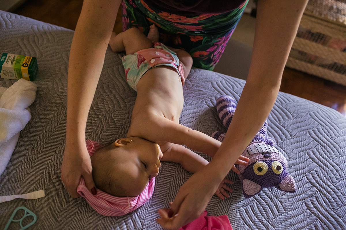 mãe colocando a roupa na sua bebê enquanto ela brinca com o gato de pelúcia, por adrianacostafotos