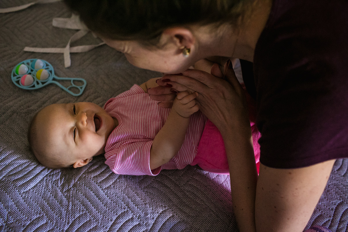 bebê sorrindo para a mãe enquanto ela termina de arrumá-la após o banho, por Adriana Costa
