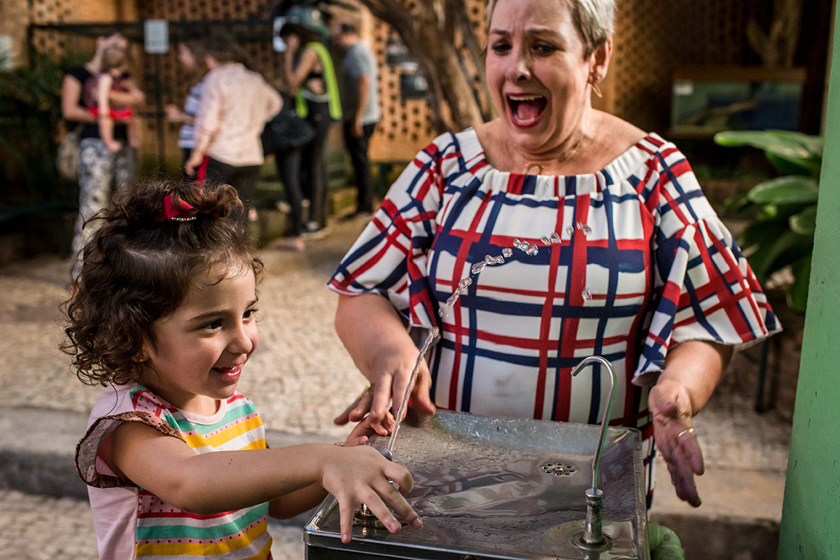 senhora dando risada da criança se molhando no bebedouro, por adrianacostafotos