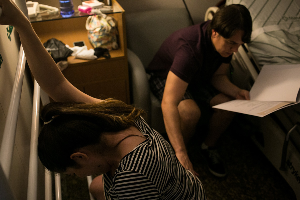 marido massageando a esposa durante trabalho de parto enquanto lê o plano de parto escrito por ela, em foto de Adriana Costa