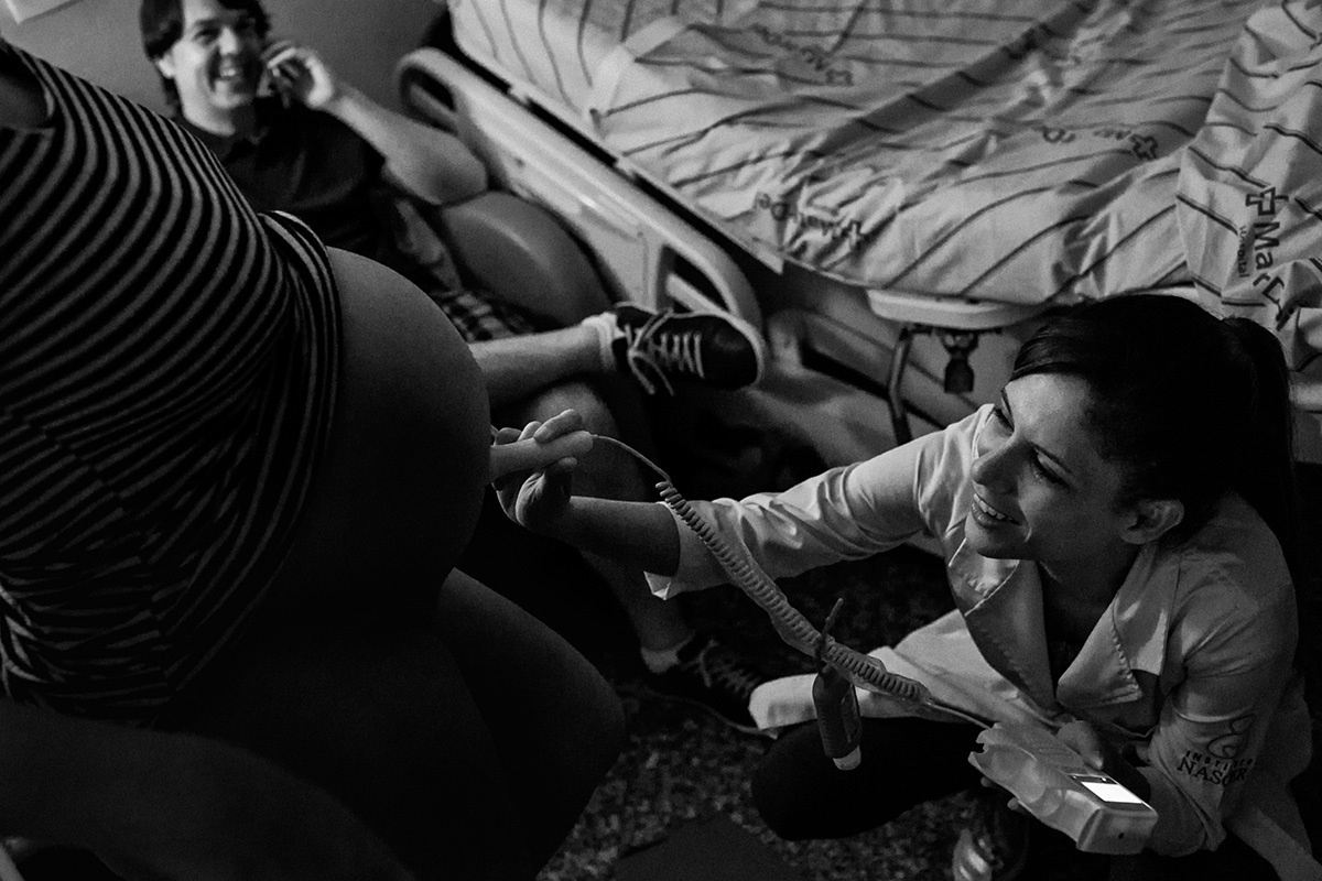 marido conversando feliz com amigos ao celular enquanto sua esposa é avaliada pela enfermeira obstétrica do Instituto Nascer.