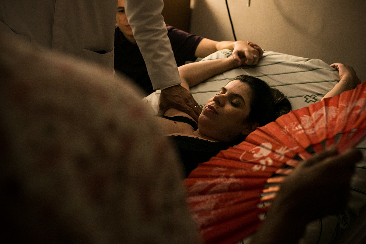 foto de Adriana Costa da gestante sendo ventilada por um leque por sua doula e recebendo o apoio de seu obstetra e também do marido