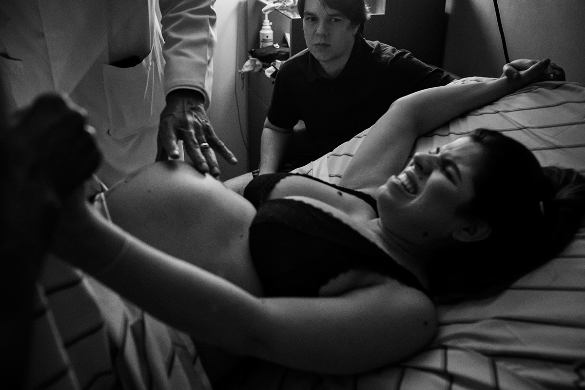 marido observando obstetra avaliando sua esposa durante uma das contrações do trabalho de parto, por Adriana Costa