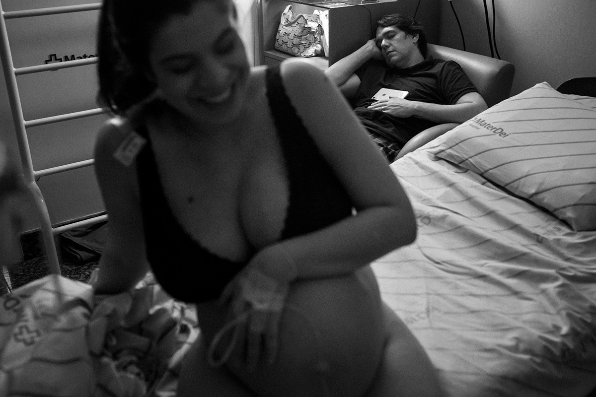 gestante rindo enquanto seu marido dorme vencido pelo cansaço durante o trabalho de parto
