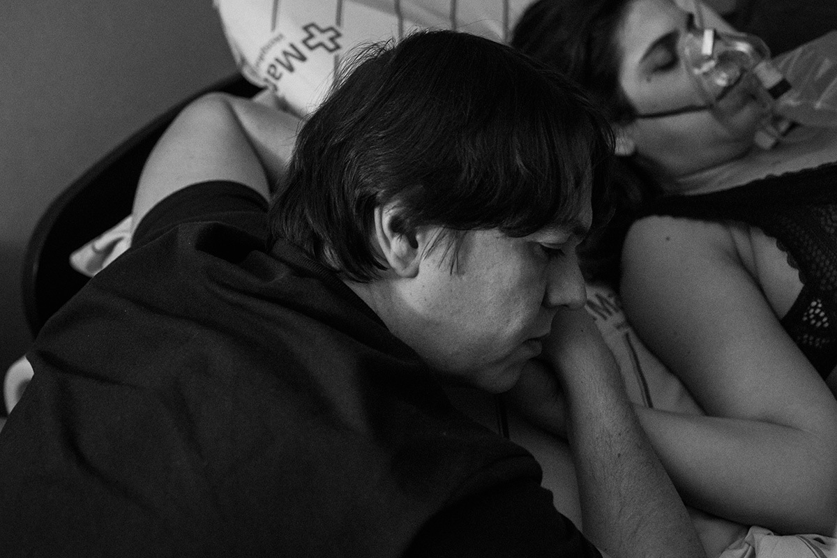 marido deitado á cabeceira da cama da parturiente enquanto ela recebe oxigênio