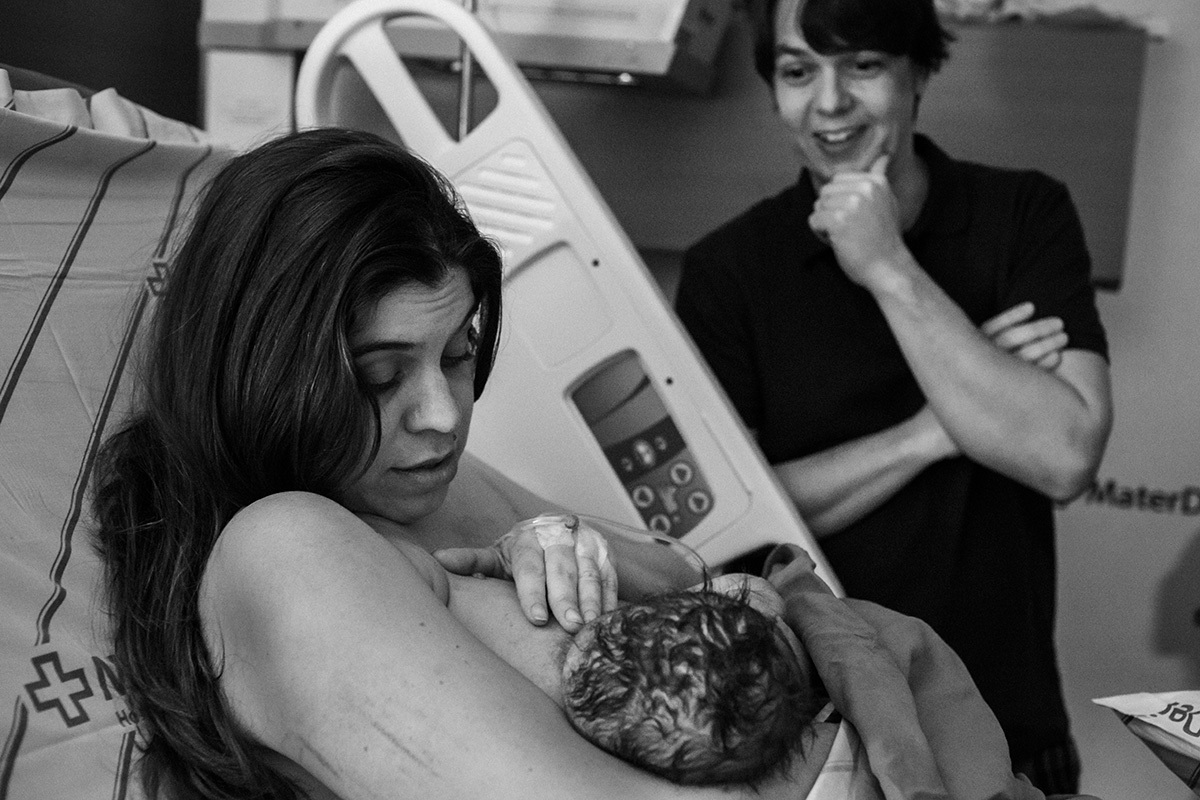 pai observa feliz e surpreso seu filho amamentando pela primeira vez