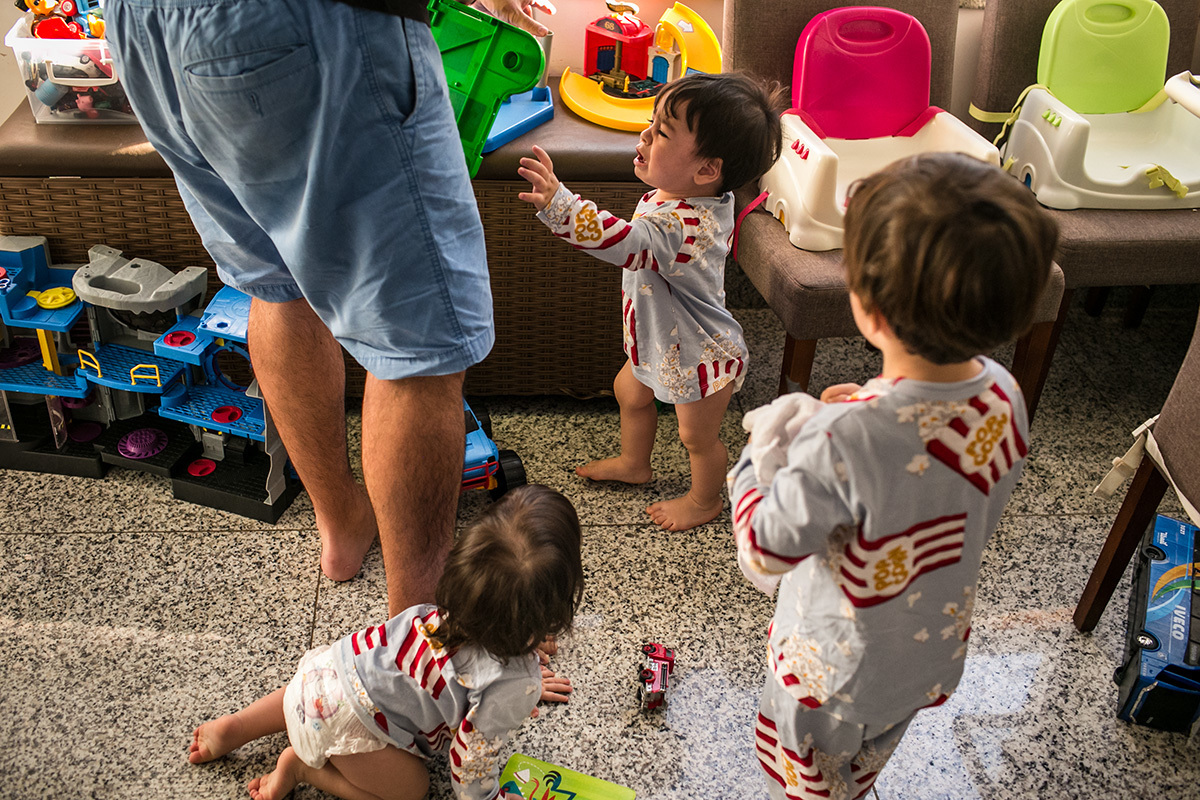 Pai ajudando seus quatro filhos pequenos num momento de choro e conflito, por Adriana Costa