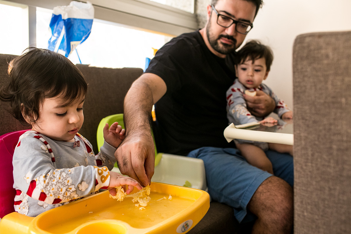 pai divide o ovo do café da manhã com uma de suas filhas gêmeas, em um documental de família feito por Adriana Costa
