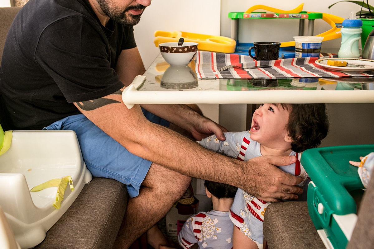 pai pega um de seus trigêmeos que chora debaixo da mesa do café da manhã, por adrianacostafotos