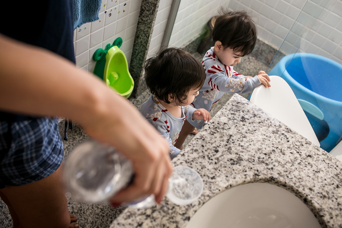 Renata Lucena prepara as seringas com soro fisiológico para lavar o nariz dos trigêmeos enquanto eles brincam no banheiro, por adrianacostafotos