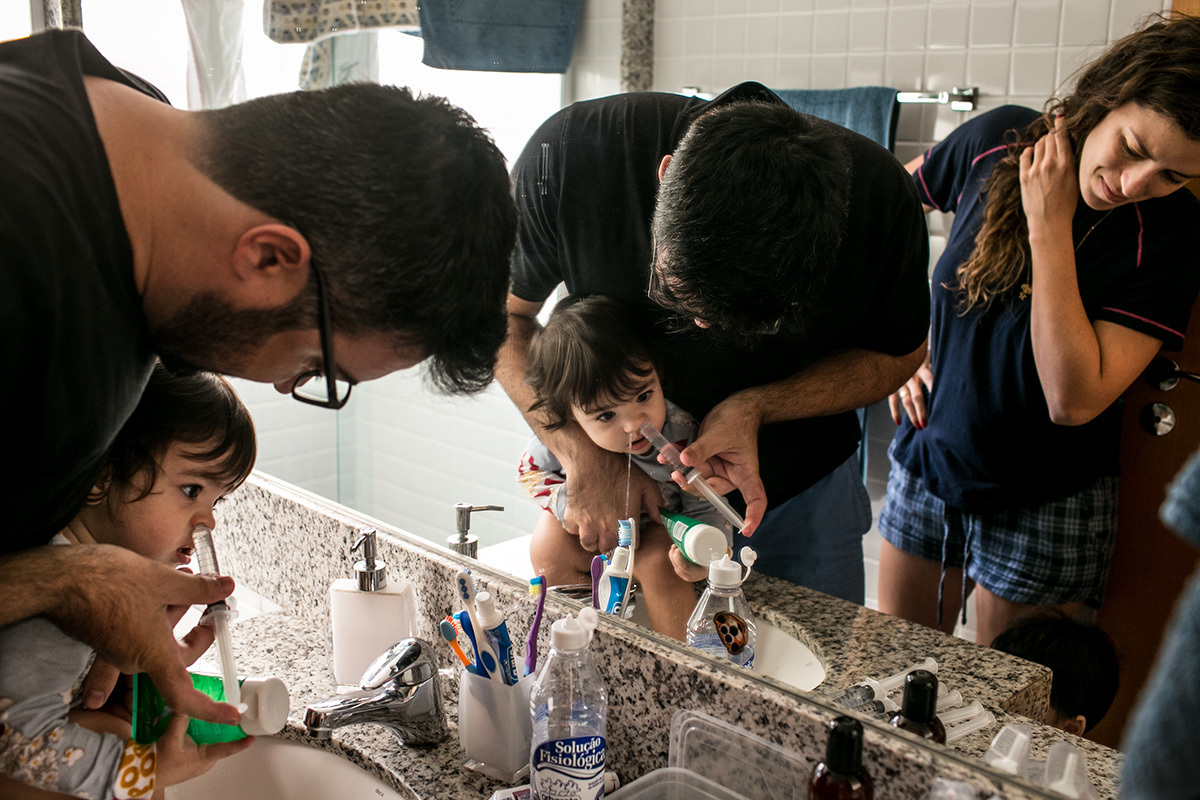 Adriana Costa fotografou Renata Lucena observando seu marido fazer a limpeza do nariz de um de seus trigêmeos com seringa e soro fisiológico