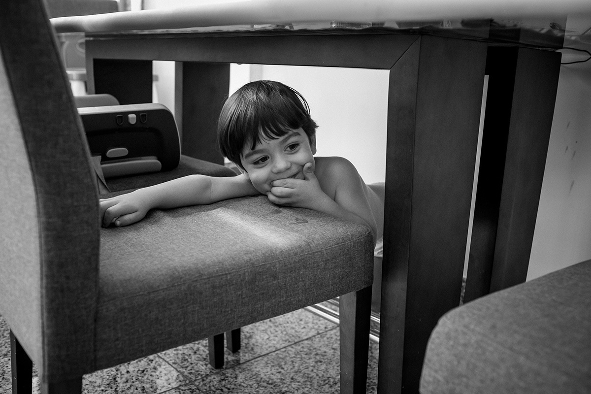 Rafinha ri brincando debaixo da mesa de sua casa, por Adriana Costa