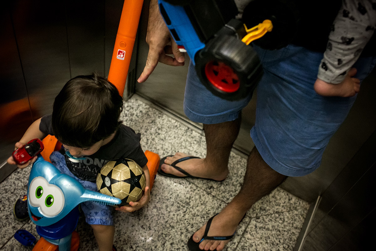pai desce cheio de brinquedos com seus filhos para o playground do prédio, por adrianacostafotos