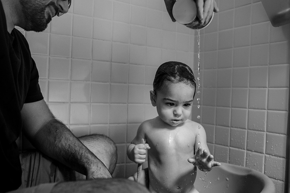 pai brinca com um de seus trigêmeos durante o banho, em foto de Adriana Costa