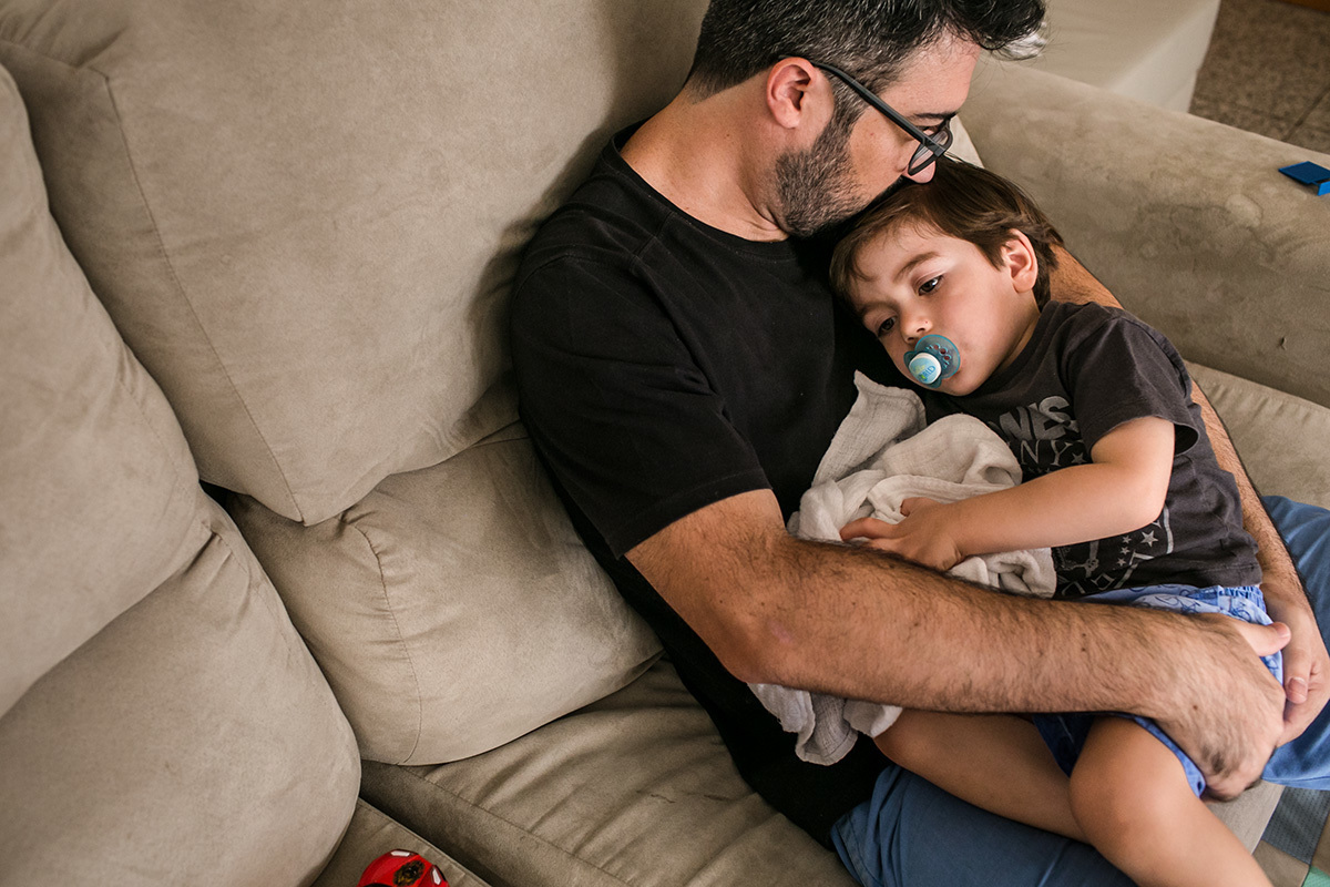 pai dá carinho ao filho que está com sono, em foto de Adriana Costa