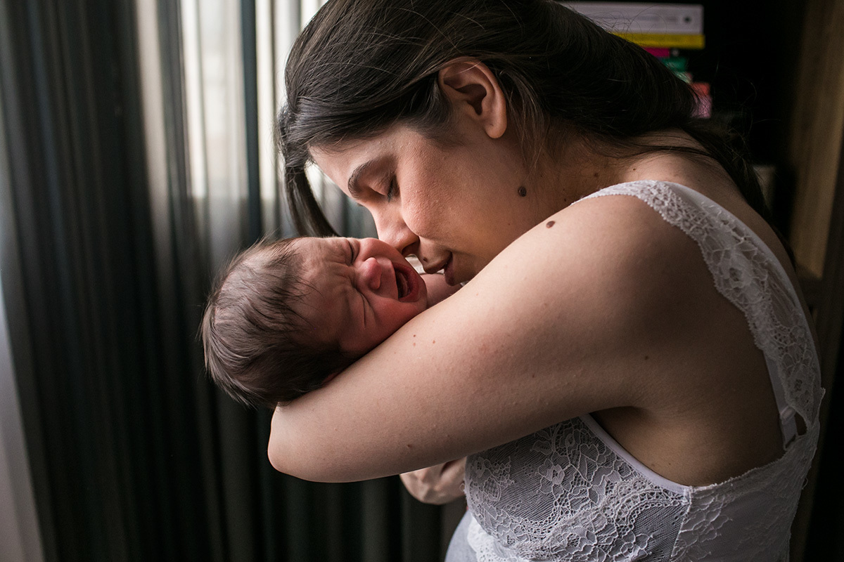 mãe canta no ouvido de seu bebê que chora para acalmá-lo durante um acompanhamento documental feito por Adriana Costa