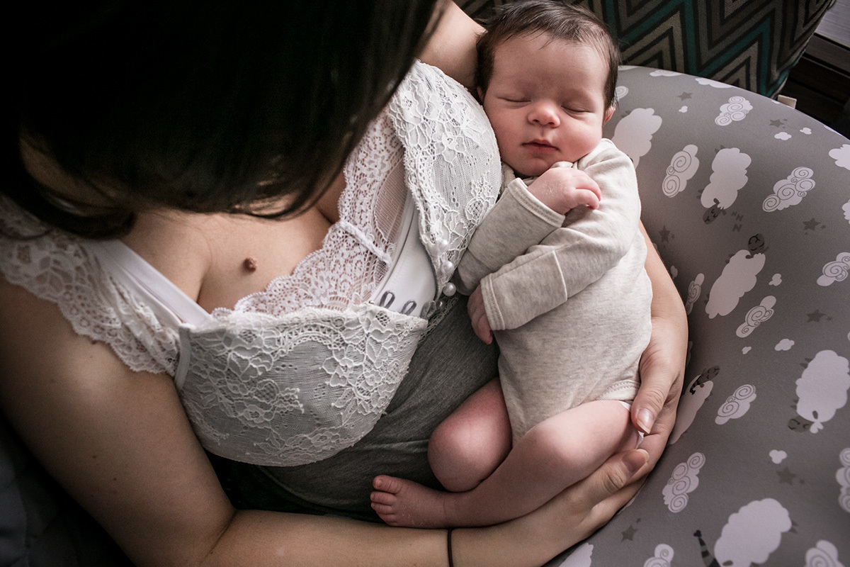 bebê dorme aconchegado no colo da mãe após amamentar, em foto de Adriana Costa