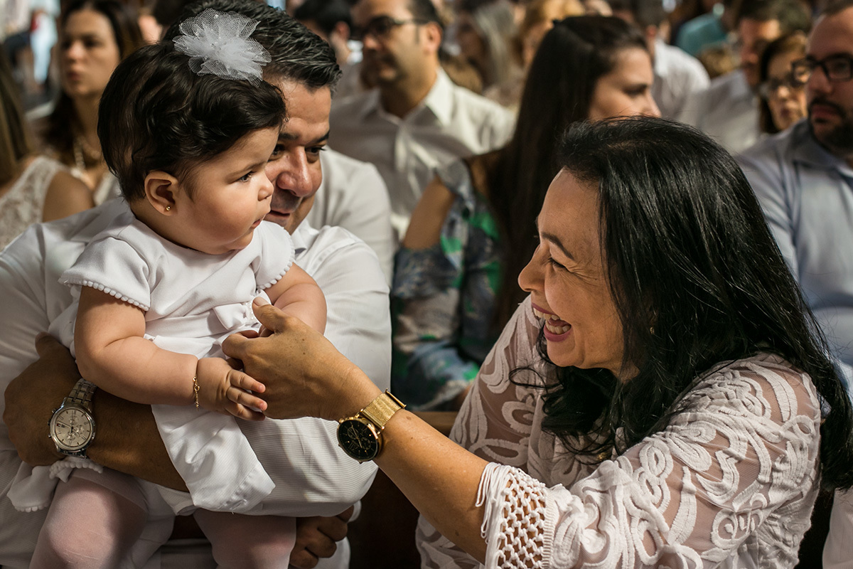 madrinha brincando com sua afilhada durante a cerimônia de batismo, por Adriana Costa
