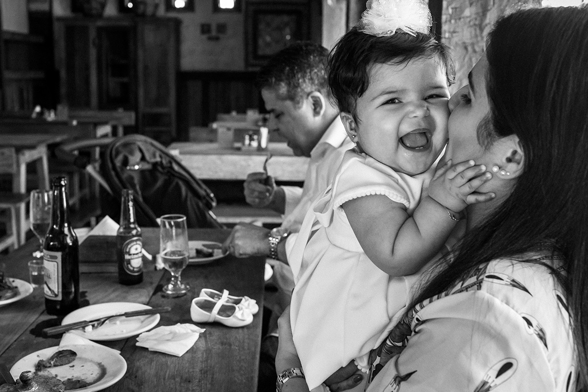 bebê sorrindo super feliz no colo da mãe durante almoço de comemoração do seu batizado, por Adriana Costa