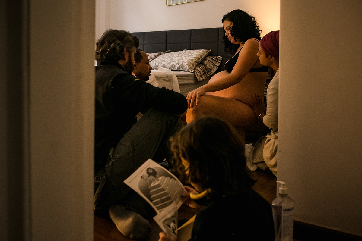 criança lê revistinha enquanto sua mãe está em trabalho de parto, em uma foto de Adriana Costa